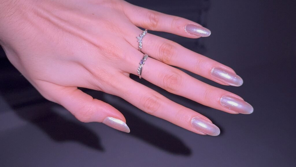 Mão com unhas amendoadas com esmalte perolado cintilante e acabamento de manicure russa.